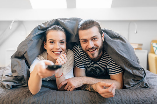Young couple laying in the bed and watching tv