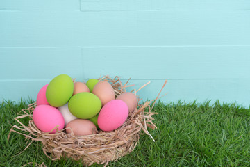 Coloeful easter eggs in nest on pastel color background with space.