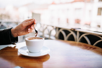 Female hand holding a spoon near the coffee cup outdoors.