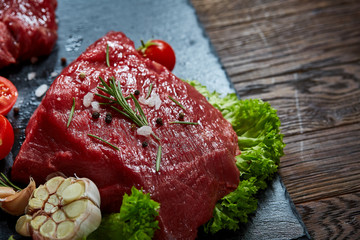 Composition of raw beefsteak on slate board with vegetables and seasoning, selective focus, close-up.