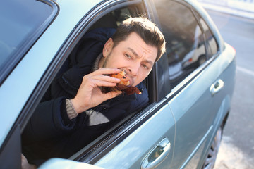 Young man eating muffin inside car in traffic jam