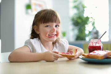 Cute little girl eating toast with jam at home
