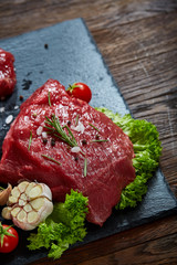 Composition of raw beefsteak on slate board with vegetables and seasoning, selective focus, close-up.