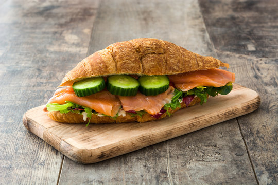 Croissant sandwich with salmon and vegetables on wooden table
