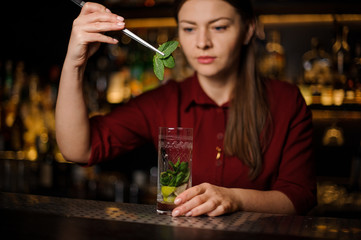 blonde barmaid in a red dress prepares a mojito adding leaves of mint