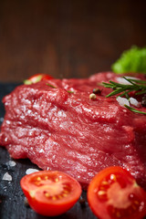 Composition of raw beefsteak on slate board with vegetables and seasoning, selective focus, close-up.