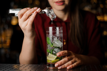 cute barmaid in a red dress prepares a mojito using ice tongs