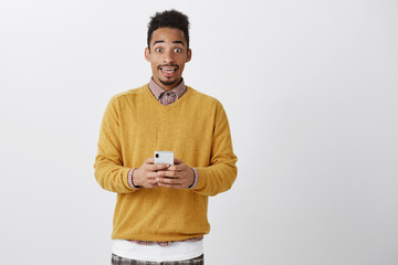 Temptation gets high between two lovers. Amazed and thrilled attractive african-american student in yellow sweater holding smartphone, reading message and being stunned, thinking what to reply