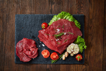 Composition of raw beefsteak on slate board with vegetables and seasoning, selective focus, close-up.