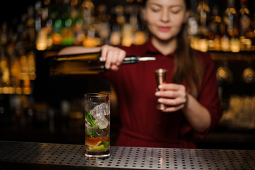 cute barmaid prepares a mojito in a crystal glass, adding dark rum