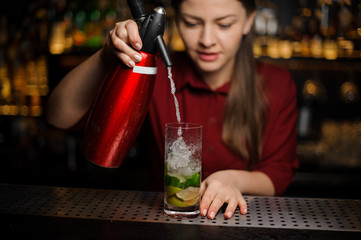 barmaid finishes preparing a mojito, adding soda water to the crystal glass