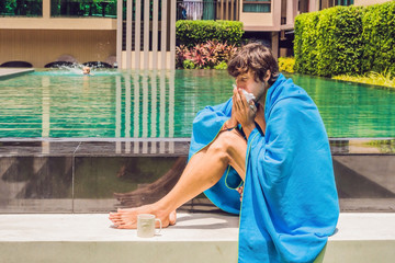 Sick man traveler. The man caught a cold on vacation, sits sad at the pool drinking tea and blows...