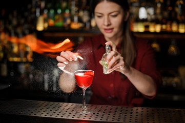bartender girl adds peat whiskey to alcoholic cocktail , spray it on a fire over a glass