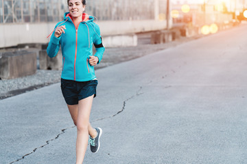 Smiling woman athlete running in city industrial area