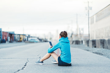Tired woman sitting after workout with mobile phone in hands