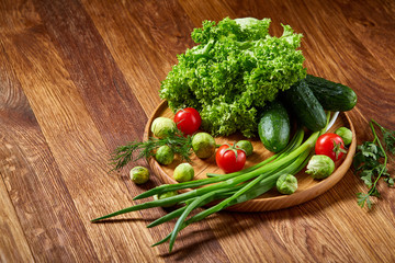 Vegetarian still life of fresh vegetables on wooden plate over rustic background, close-up, flat lay.