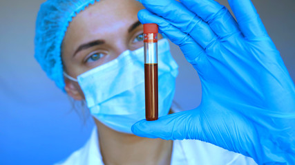 Fototapeta premium Young beautiful woman, nurse, doctor, wearing a mask, cap, test tube, tests, DNA, blue rubber gloves, white blue background.