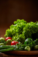 Vegetarian still life of fresh vegetables on wooden plate over rustic background, close-up, flat lay.