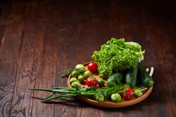 Vegetarian still life of fresh vegetables on wooden plate over rustic background, close-up, flat lay.