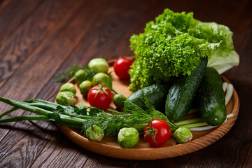 Vegetarian still life of fresh vegetables on wooden plate over rustic background, close-up, flat lay.