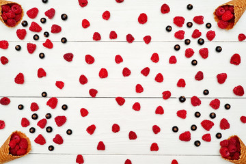 Top view of sweet fresh organic raspberries and black currants in waffle cone with free blank space. Fresh berries in cone on white wooden background. Summer and healthy food concept