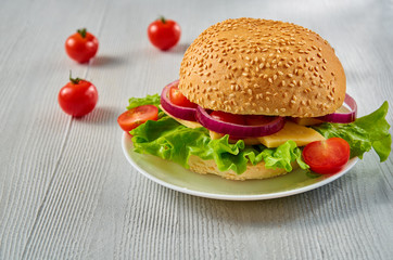 Veggie burger with salad, onion rings decorated with fresh cherry tomatoes on the gray concrete background with free copy space. Vegetarian sandwich. Side view