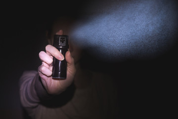 a woman is protected by a gas pepper spray in the dark, a black background. concept of safety and...