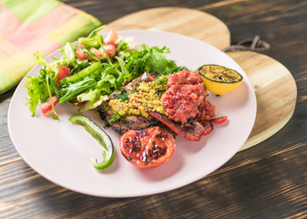 Grilled meat and salad of fresh vegetables on a plate on a wooden background.