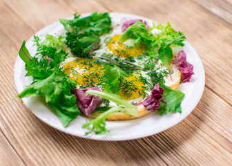 Fried eggs with greens on a plate on a wooden background. Healthy breakfast.