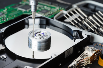 Disassembled hard disk drive inside close-up, spindle, actuator arm, read write head, platter, disassembly tools