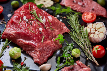 Flat lay of raw beefsteak with vegetables, herbs and spicies on metal tray, close-up, selective focus