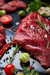 Flat lay of raw beefsteak with vegetables, herbs and spicies on metal tray, close-up, selective focus