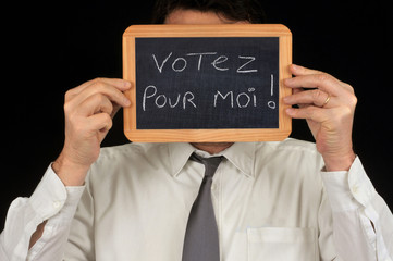 Homme cachant son visage avec une ardoise sur laquelle est écrit votez pour moi