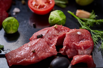 Flat lay of raw beefsteak with vegetables, herbs and spicies on metal tray, close-up, selective focus