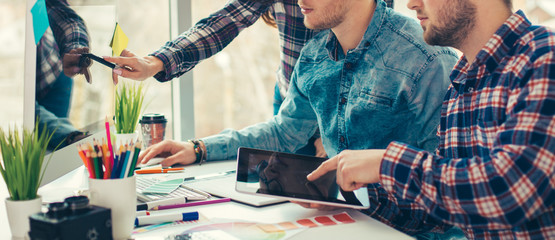 Group of international university students having fun studying in library, three colleagues of modern work co-working space talking and smiling while sitting at the desk table with laptop computer