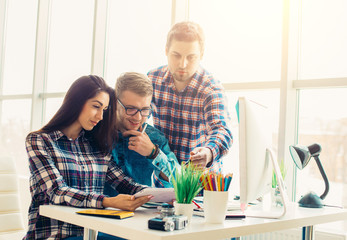 Obraz premium Side view of three creative designer artists working on computer at the office
