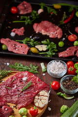 Still life of raw beef meat with vegetables on wooden plate over vintage background, top view, selective focus