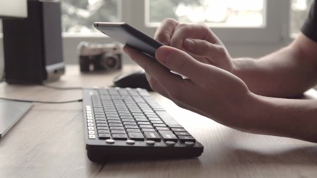 Young man using tablet while sitting computer keyboard and mouse. Freelancer photographer working and using tablet for communication with clients.