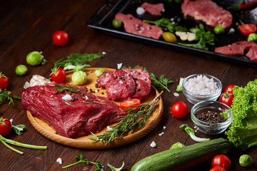 Still life of raw beef meat with vegetables on wooden plate over vintage background, top view, selective focus