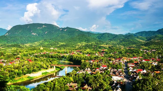 Luang Prabang, Laos. Aerial view of Luang Prabang town in Laos. Cloudy sky over the small city surrounded by mountains. Car traffic and river. Time-lapse in the evening