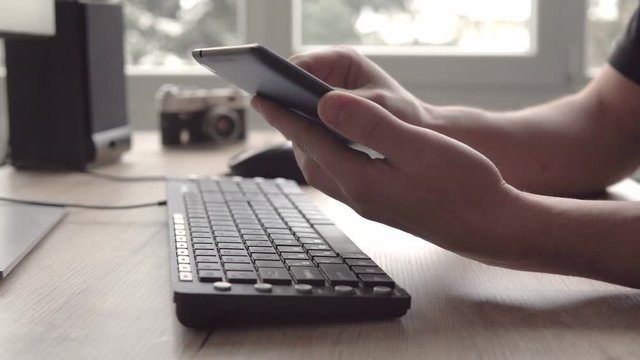 Young man using tablet while sitting computer keyboard and mouse. Freelancer photographer working and using tablet for communication with clients.