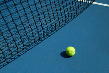 Yellow tennis ball is laying near black opened tennis court's net. Contrast image with satureted colors and shadows. Concept of tennis outfit photografing.