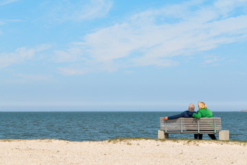 Fototapeta na wymiar Couple sitting on bench and looking at the sea