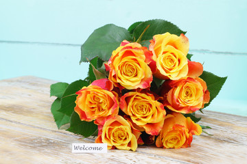 Welcome card with orange rose bouquet on wooden surface
