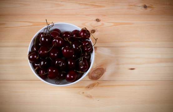 Red ripe cherries berries in bowl on  wooden background. Top view with copy space.