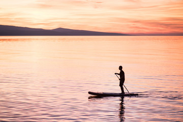 Silhouette of man at sunset standing on paddle board. Summer beach leisure activity. Active healthy lifestyle and travel summer concept