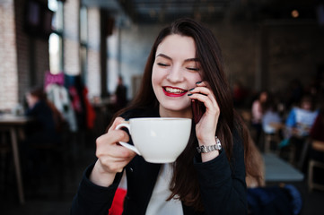 Brunette girl sitting on cafe with cup of cappuccino and speaking mobile phone.