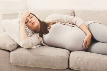 Young pregnant woman with headache lying on sofa