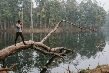 Fototapeta na wymiar Traveller photographer standing on big tree and do pictures of tropical lake landscape