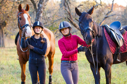 Two teenage girls with their horses in autumn park. Equestrian sport background with copy space